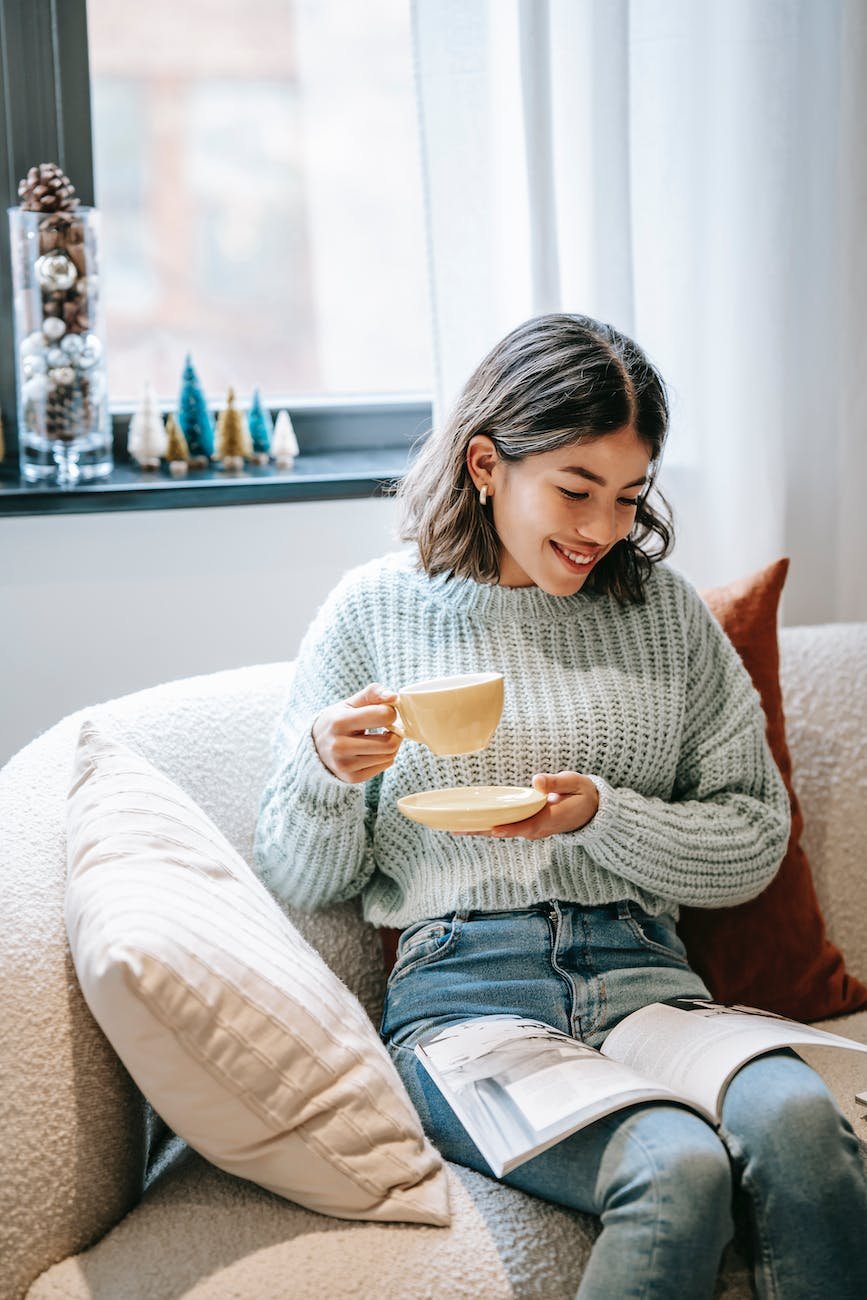 smiling asian woman reading magazine and enjoying hot coffee
